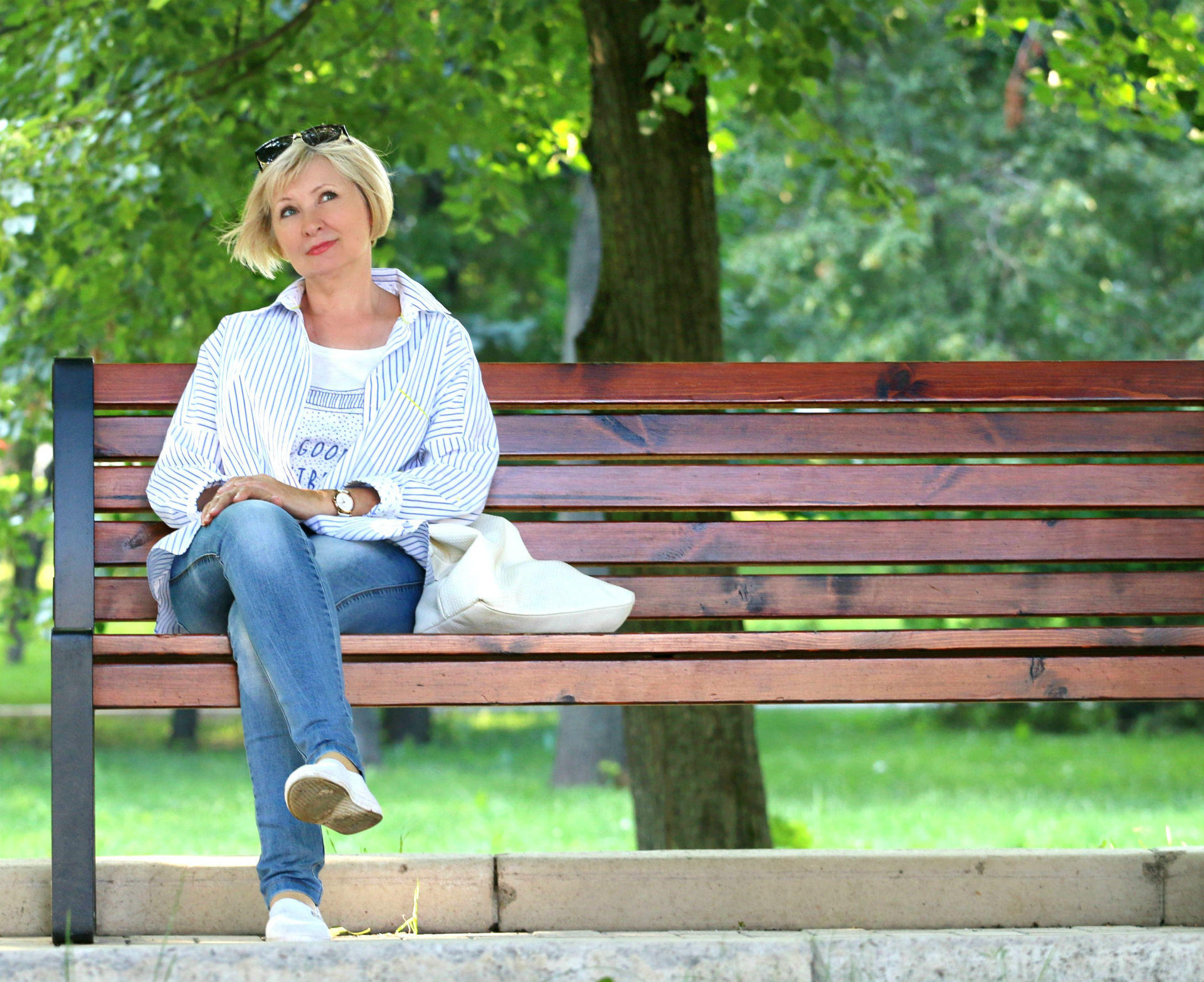 blond women sitting on a bench starting at the sky