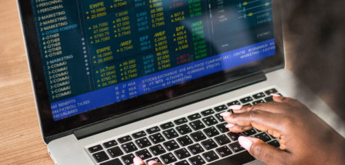 women looking at a computer screen that displays the colorful stock market