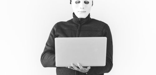 hacker with a face mask on holding a laptop