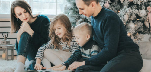 family of four reading a book around a christmas tree